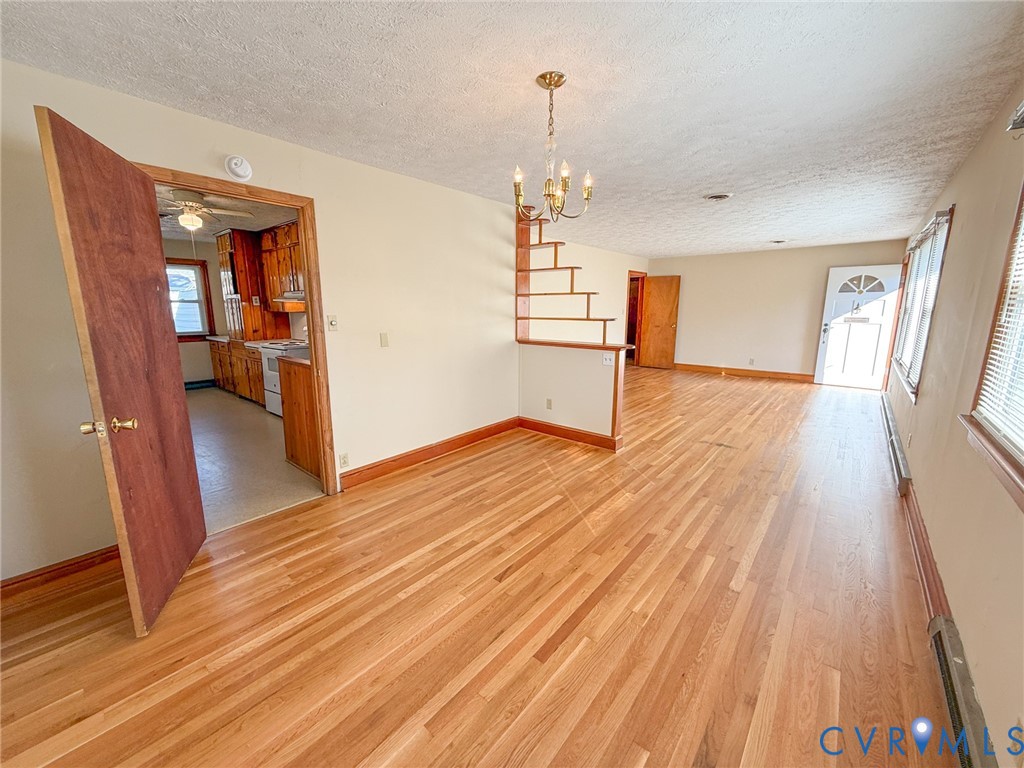 Open-concept interior featuring light-toned wood-finish flooring, a tiered open-frame wooden partition, a multi-light candelabra chandelier, and a solid wood entry door