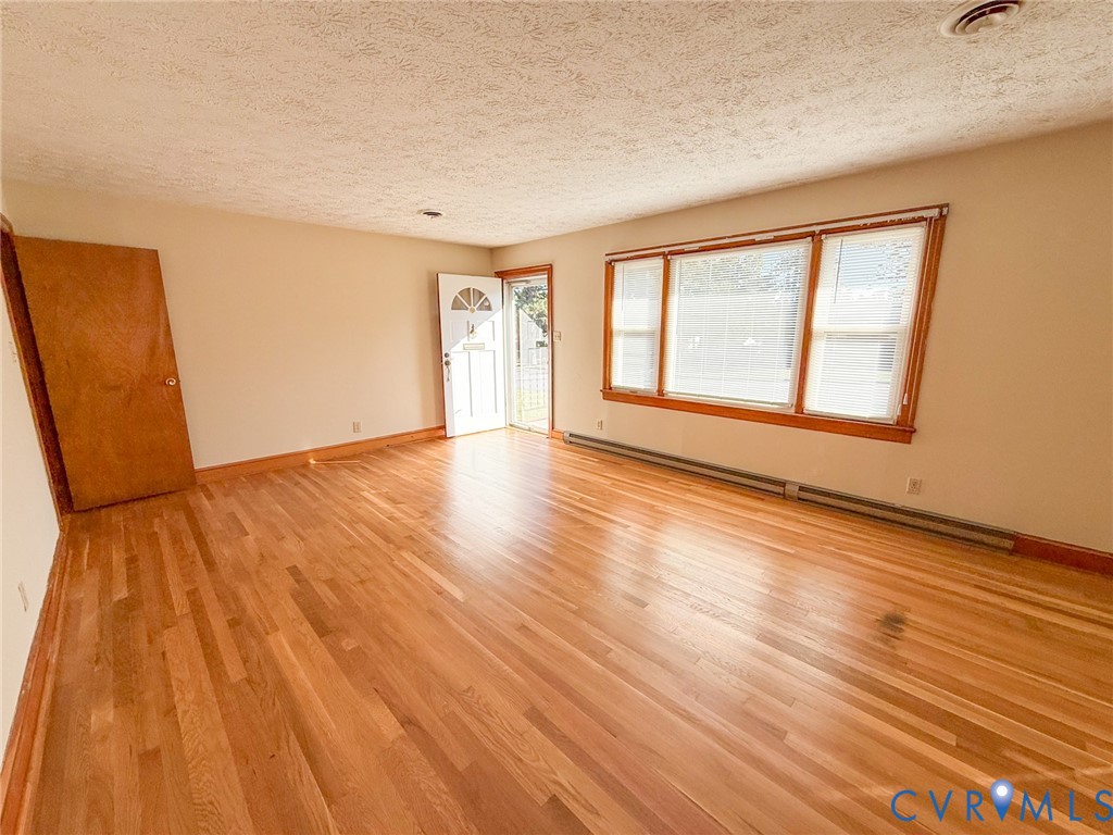 Interior space featuring polished wood-finish flooring, large triple-pane windows with wood-toned trim, and a solid wood entry door with a decorative glass panel