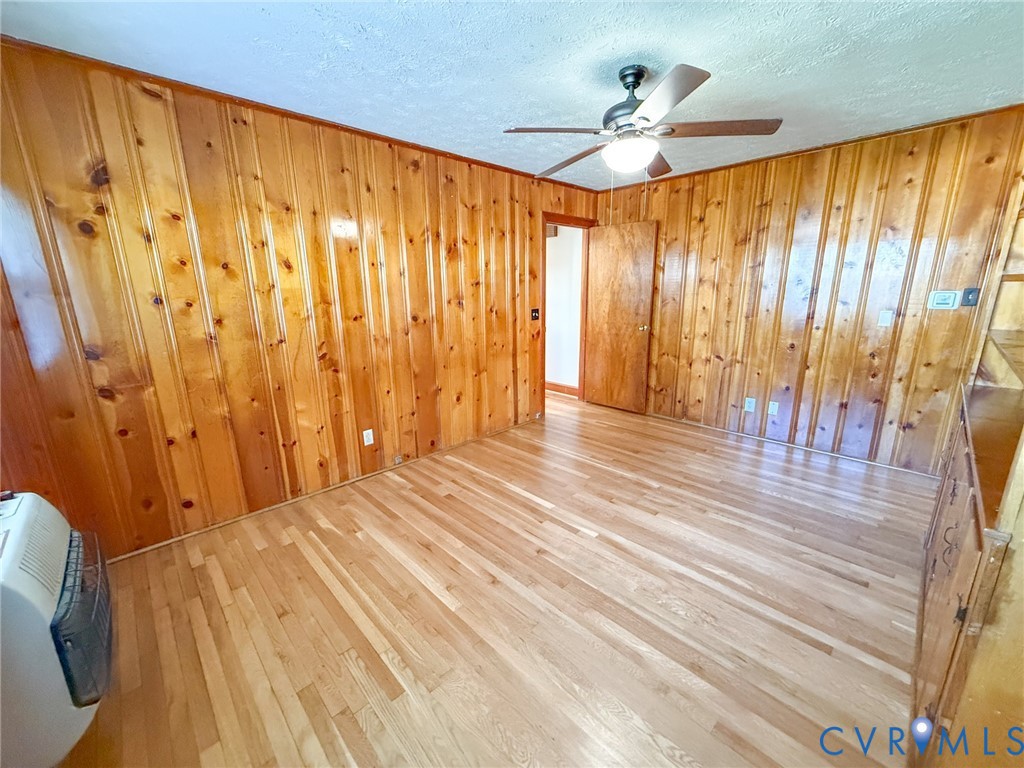 Interior space featuring vertical wood-paneled walls, wood-finish flooring, and a ceiling fan with integrated lighting