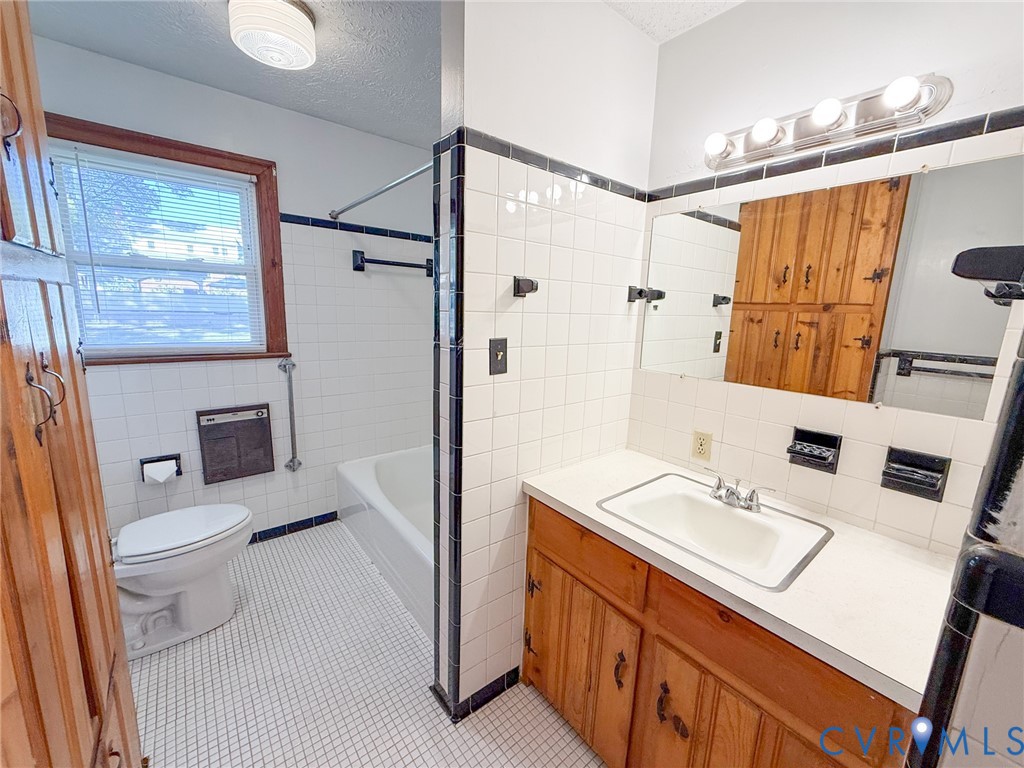Bathroom featuring a vanity with integrated sink and countertop, full-height tile wall surround, built-in natural wood cabinetry, and a combination tub and shower