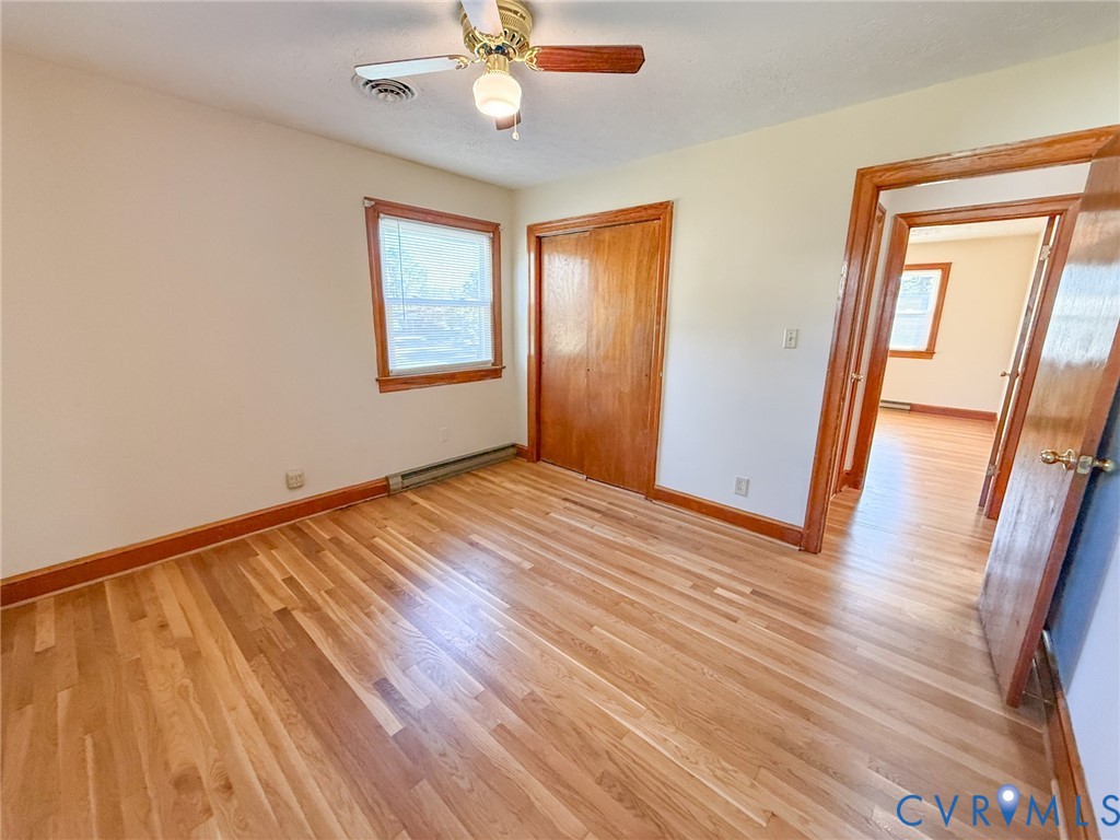 Wood-finish flooring, double-door wood closet, ceiling fan with integrated lighting, and natural wood trim surrounding the door and window frame