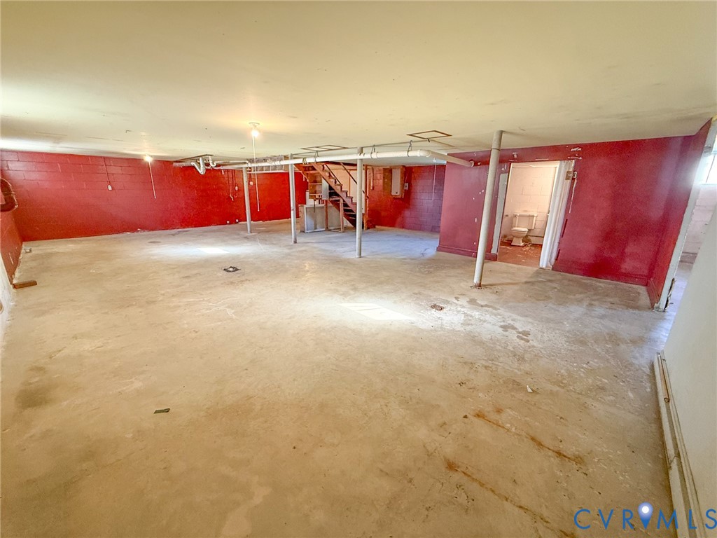 Open-concept interior space featuring painted masonry walls, concrete flooring, exposed ceiling structural elements, support columns, and an enclosed room with a toilet