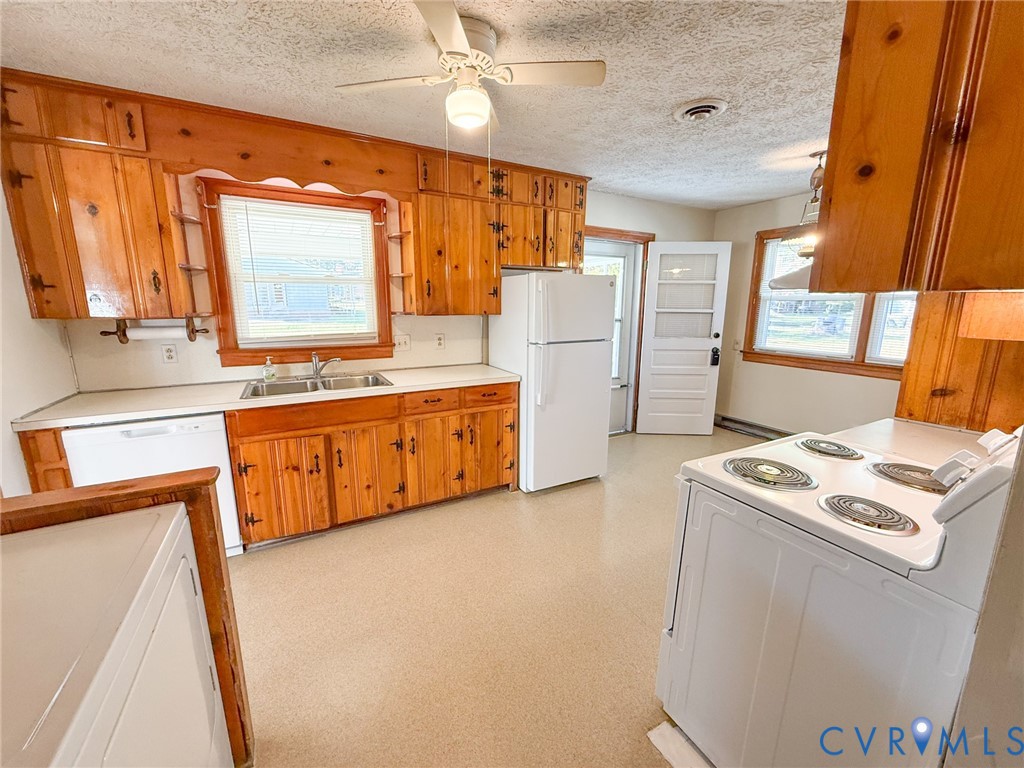 Kitchen featuring knotty pine cabinetry, a dual-basin stainless steel sink, solid-surface countertops, and a ceiling-mounted light fixture with a fan