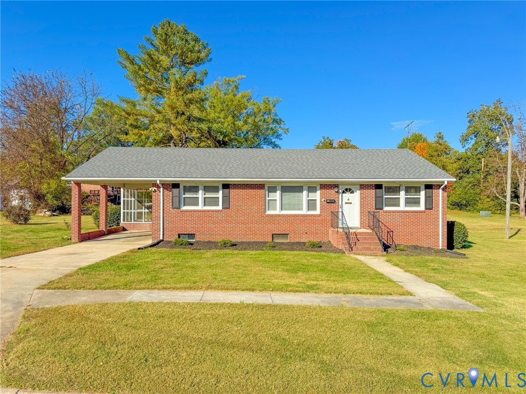 Brick exterior ranch home featuring a covered carport, pitched asphalt shingle roof, dark window shutters, and a front entry staircase with metal handrails
