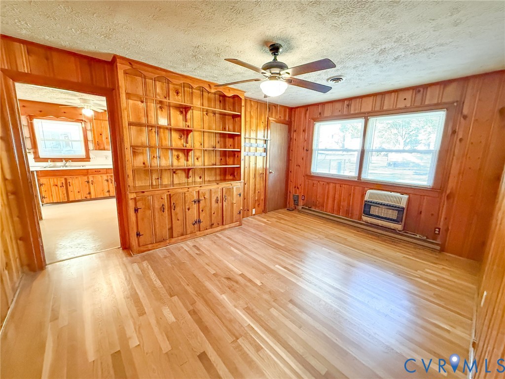 Wood-panelled interior featuring wood-finish flooring, built-in wooden shelving, a ceiling fan with integrated light fixture, and large multi-pane windows
