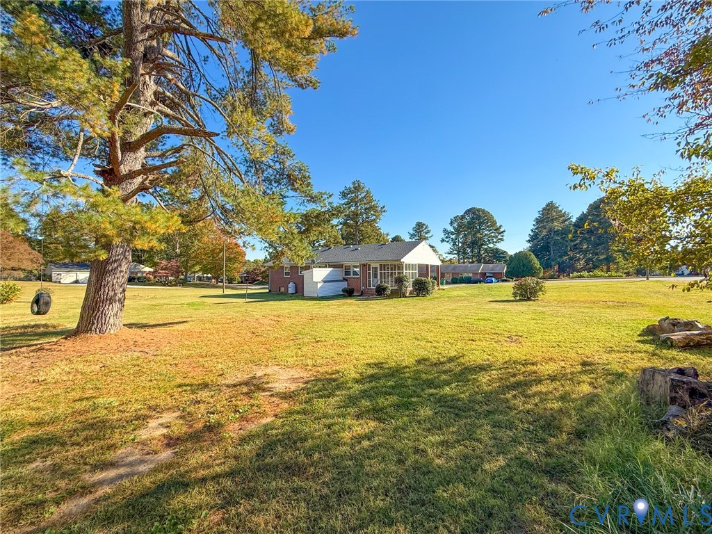 Expansive grassy lot featuring a brick-exterior residence, a covered patio, and large mature trees