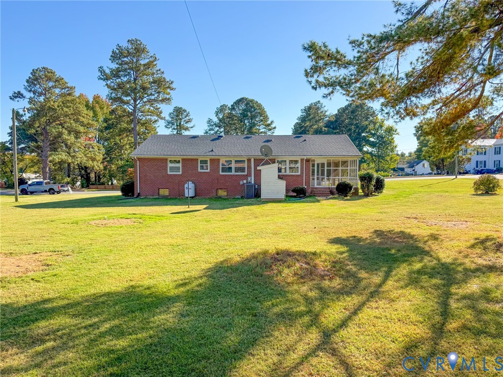 Brick exterior residence featuring an expansive lawn, asphalt shingle roof, and a screened-in porch
