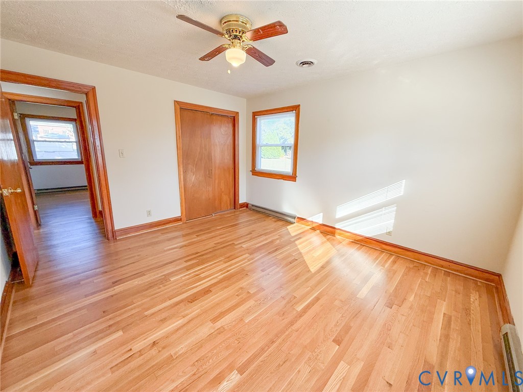 Room featuring wood-finish flooring, wood-trim window casings, wood-door closet, and ceiling fan with integrated light fixture