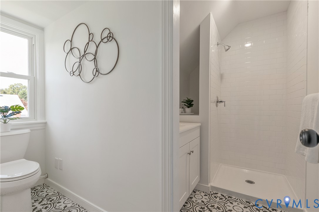 Bathroom featuring a shower stall with white subway tile surround, vanity with cabinetry, and patterned floor tile