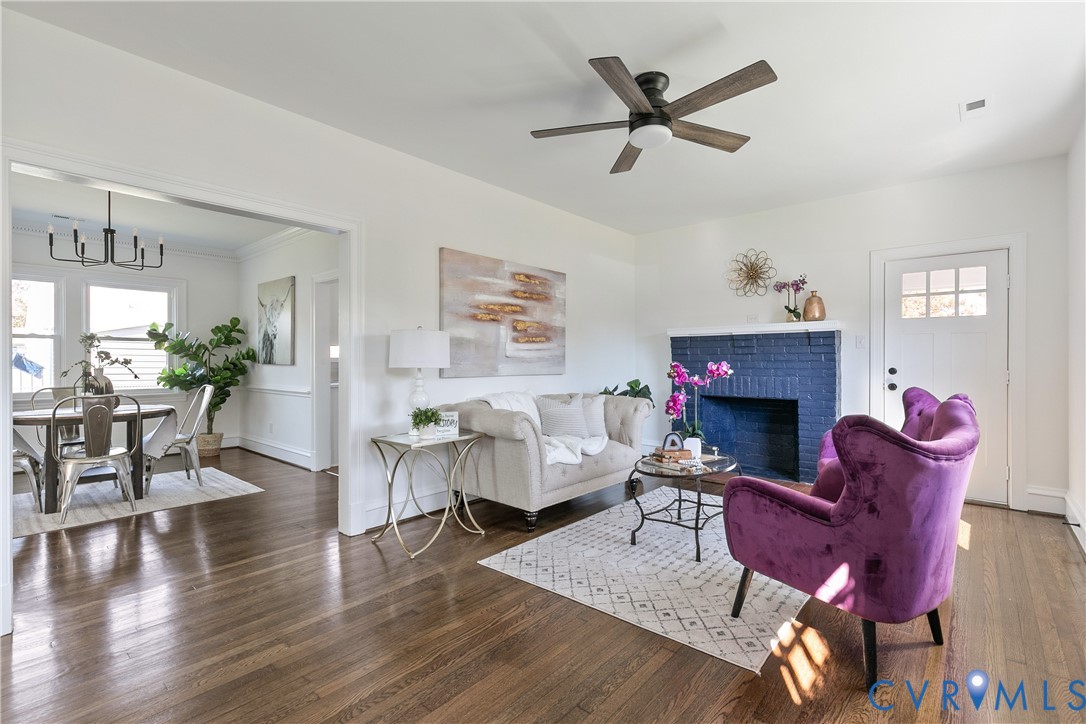 Living area featuring dark wood-finish flooring, a painted brick fireplace, a ceiling fan, and a six-pane entry door