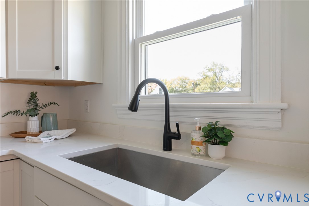 Undermount stainless steel kitchen sink featuring a matte black high-arc pull-down faucet, white stone-composite countertops, and white shaker-style cabinetry