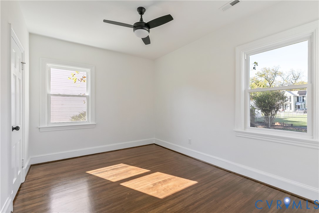 Room featuring wood-finish flooring, dual windows, and a matte black ceiling fan