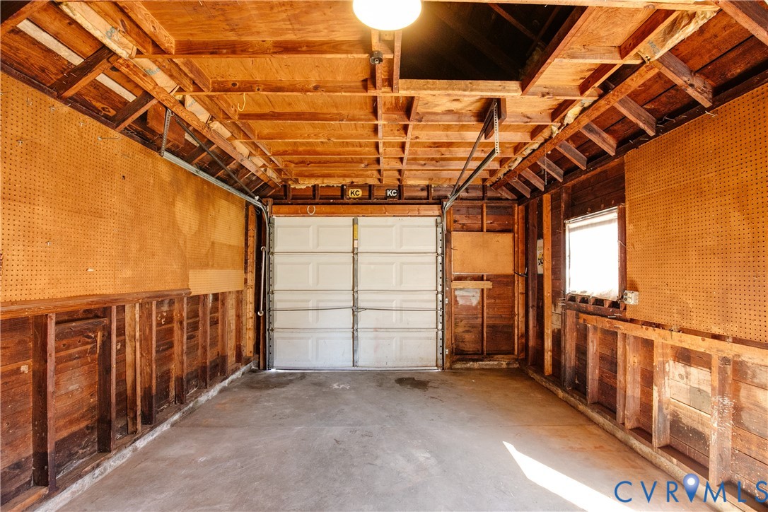 Detached garage featuring exposed wood-stud framing, pegboard wall panels, a concrete floor, an overhead sectional garage door, and a single window