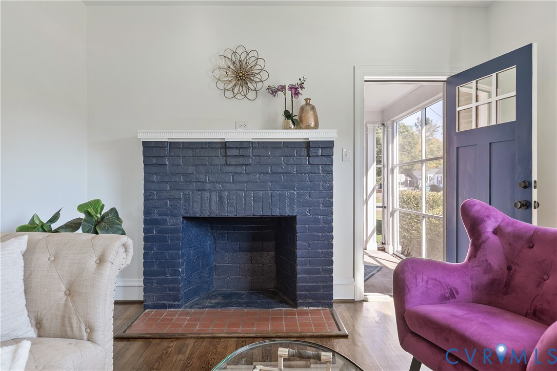 Painted brick fireplace with a white mantelpiece, terracotta hearth, wood-finish flooring, and a multi-pane glass entry door