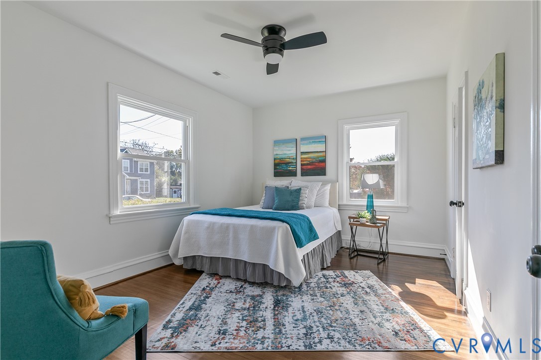 Bedroom featuring wood-finish flooring, dual windows, and a matte black ceiling fan