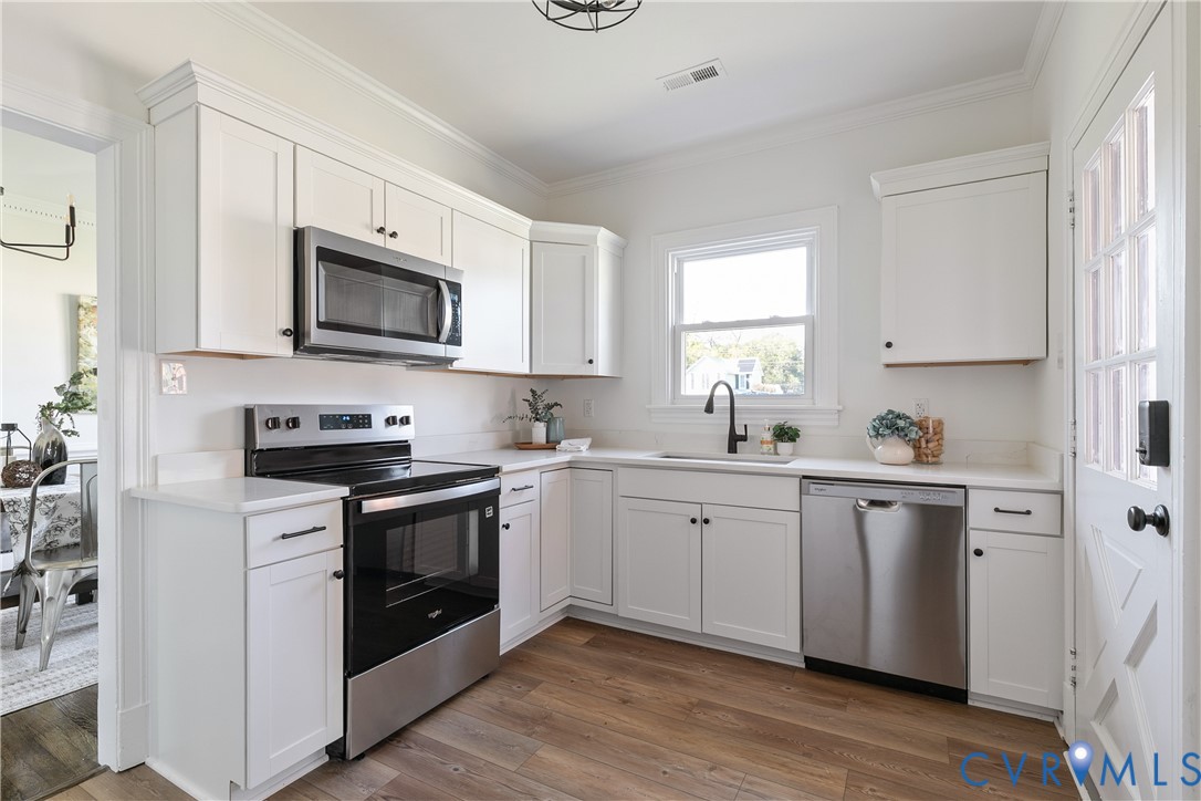 Kitchen featuring white shaker-style cabinetry, solid-surface countertops, stainless steel appliances, matte black plumbing fixtures, and wood-finish flooring