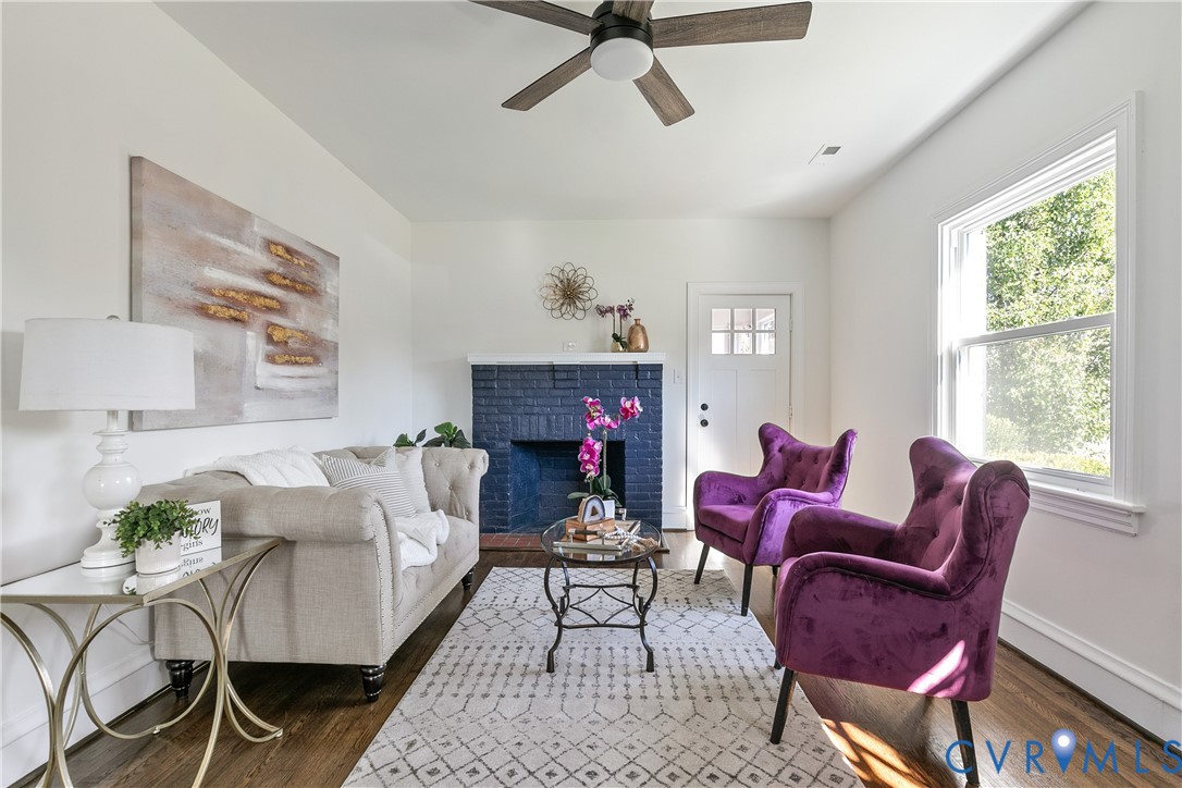 Painted brick fireplace, wood-finish flooring, ceiling fan with integrated lighting, and multi-pane window