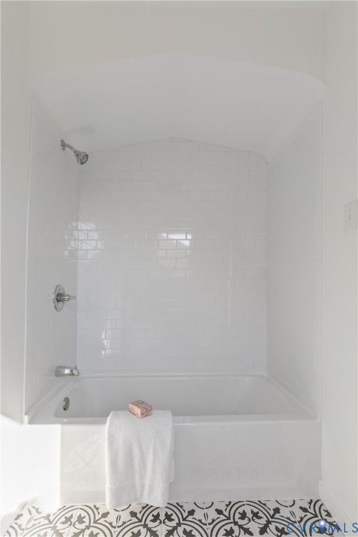Alcove bathtub featuring white subway tile surround, arched ceiling detail, polished chrome plumbing fixtures, and patterned tile flooring