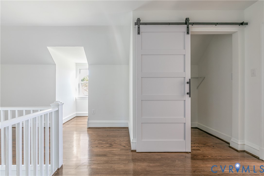 White five-panel sliding barn door with matte black hardware, wood-finish flooring, and white railing featuring a vertical baluster design
