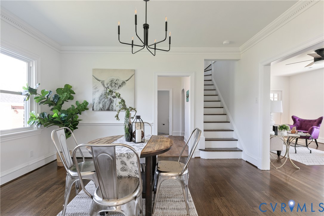 Wood-finish flooring, crown molding, chair rail trim, black metal six-light chandelier, and a painted wooden staircase