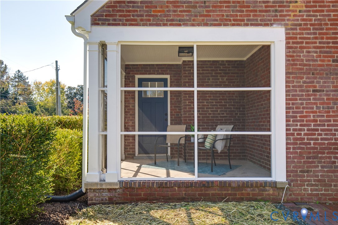 Screened porch featuring brick exterior walls, a concrete floor, beadboard ceiling, and a paneled entry door