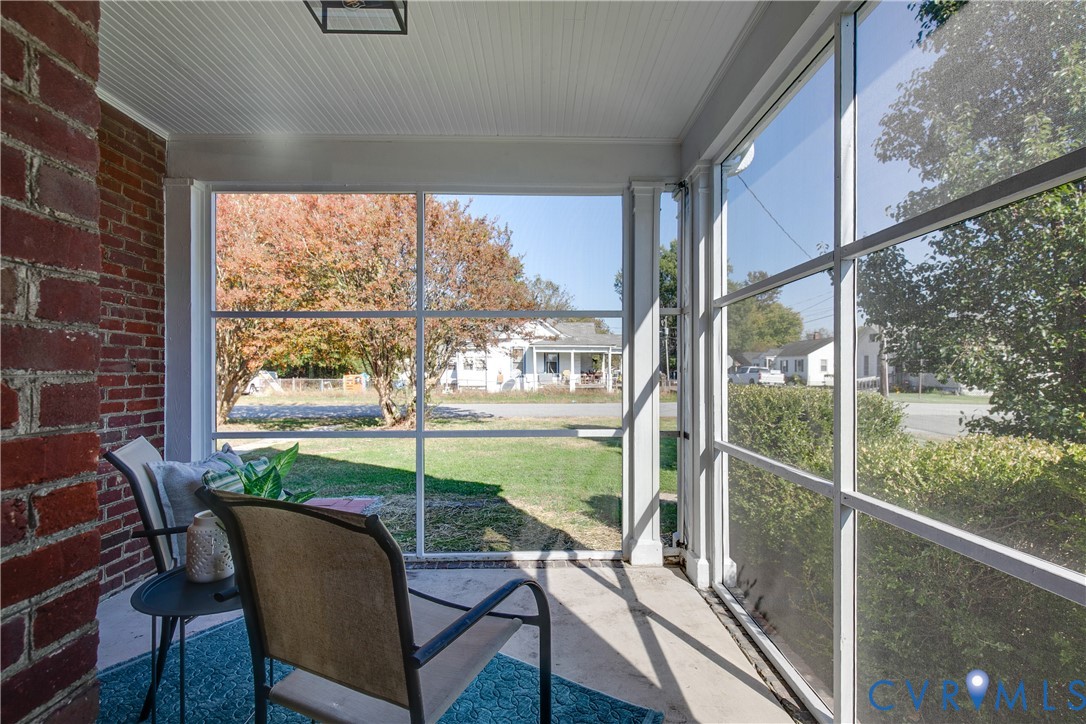 Screened-in porch featuring a concrete floor, beadboard ceiling, brick accent wall, and white structural columns
