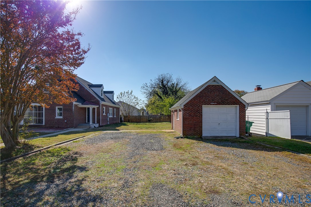 Brick exterior residence featuring a detached brick garage, gravel parking area, and mature landscaping
