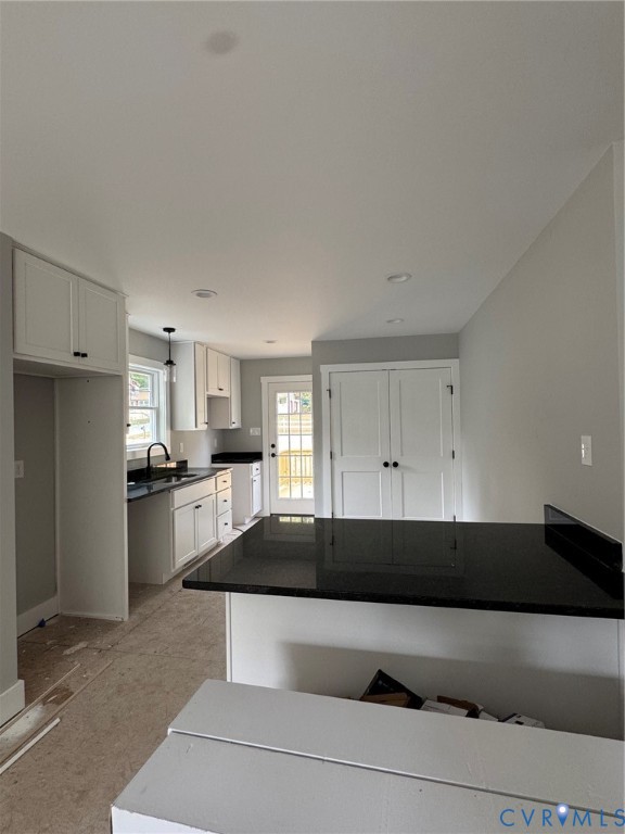 Kitchen featuring white shaker-style cabinetry, dark stone-finish countertops, a breakfast bar, recessed lighting, and a glass-paneled exterior door