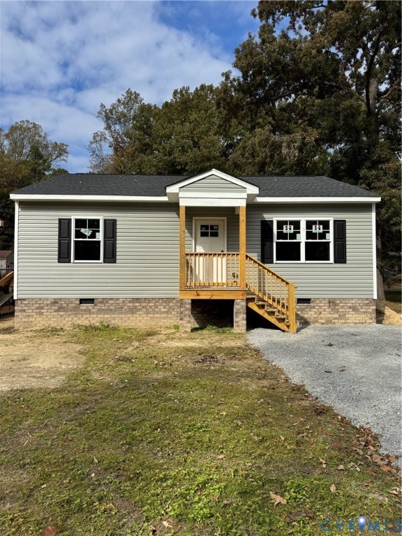 Exterior facade featuring light gray vinyl siding, a brick foundation, a covered front porch with wooden railings, and black window shutters