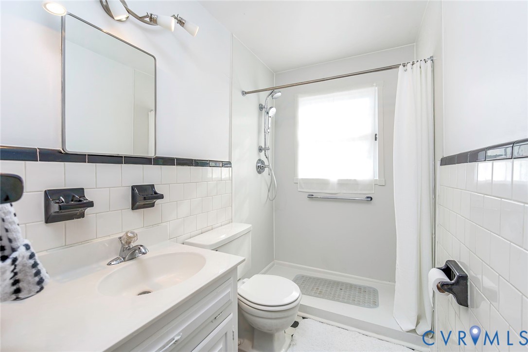 Bathroom featuring white subway tile wall accents, a vanity with a white countertop and integrated sink, a walk-in shower with a handheld fixture, and a wall-mounted medicine cabinet