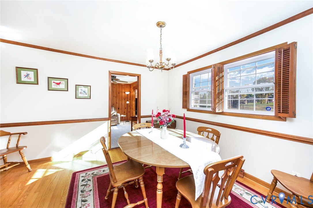 Dining area featuring wood-finish flooring, wood chair rail molding, dual windows with wood-finish shutters, and a multi-arm chandelier