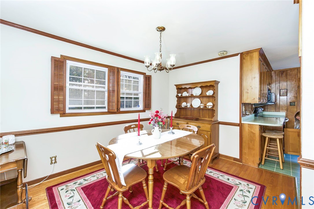 Dining space featuring wood-finish flooring, wood-toned chair rail molding, dual windows with wood shutters, and a multi-arm chandelier
