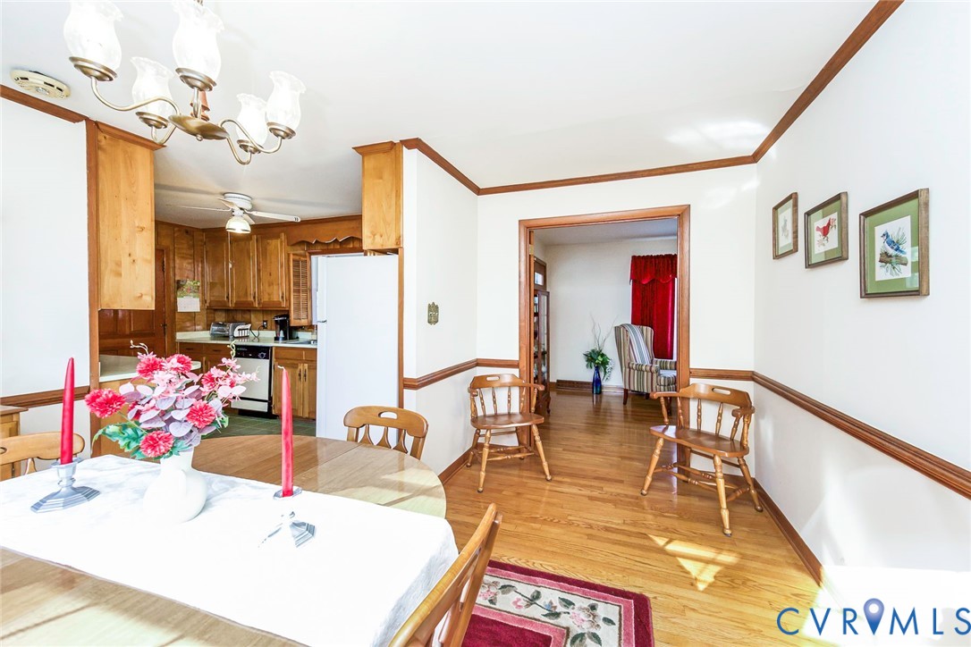 Dining area featuring wood-finish flooring, chair rail molding, and a multi-arm chandelier, encompassing a kitchen with wood cabinetry and a ceiling fan