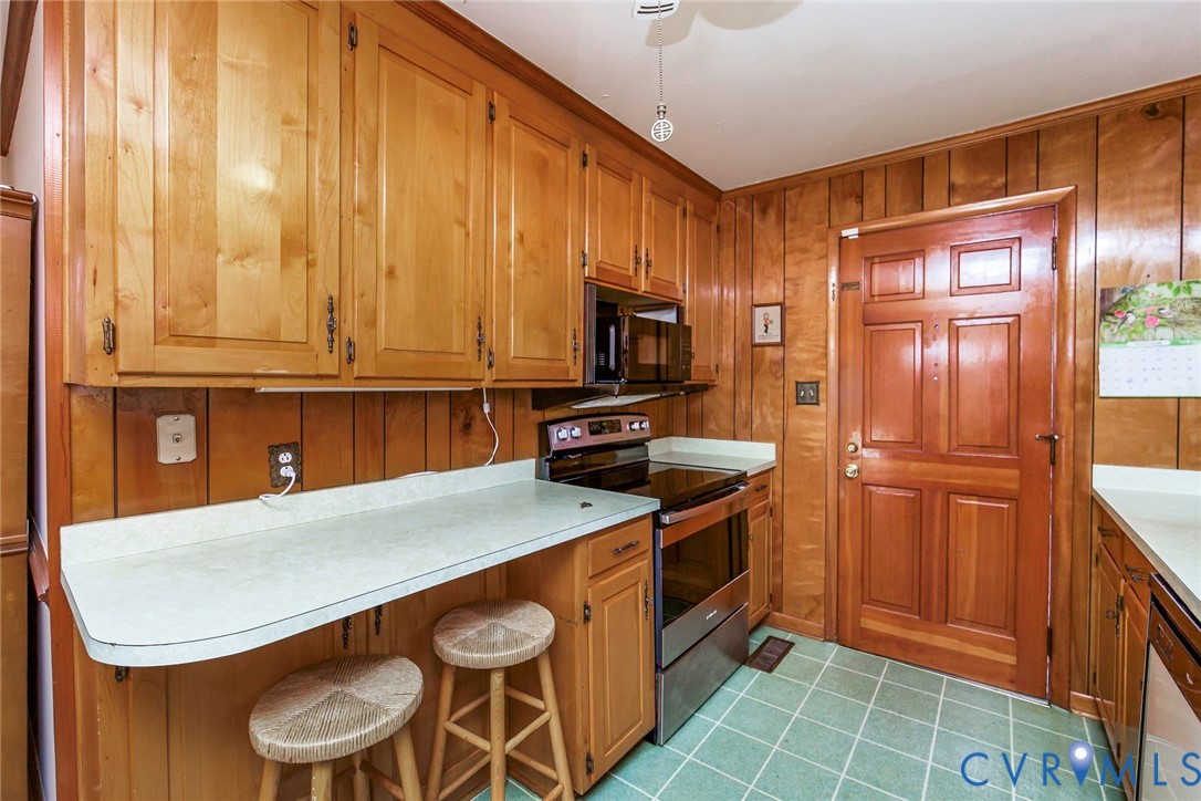 Kitchen featuring wood cabinetry, natural wood-paneled walls, solid-surface countertops, and a stainless steel built-in range and microwave