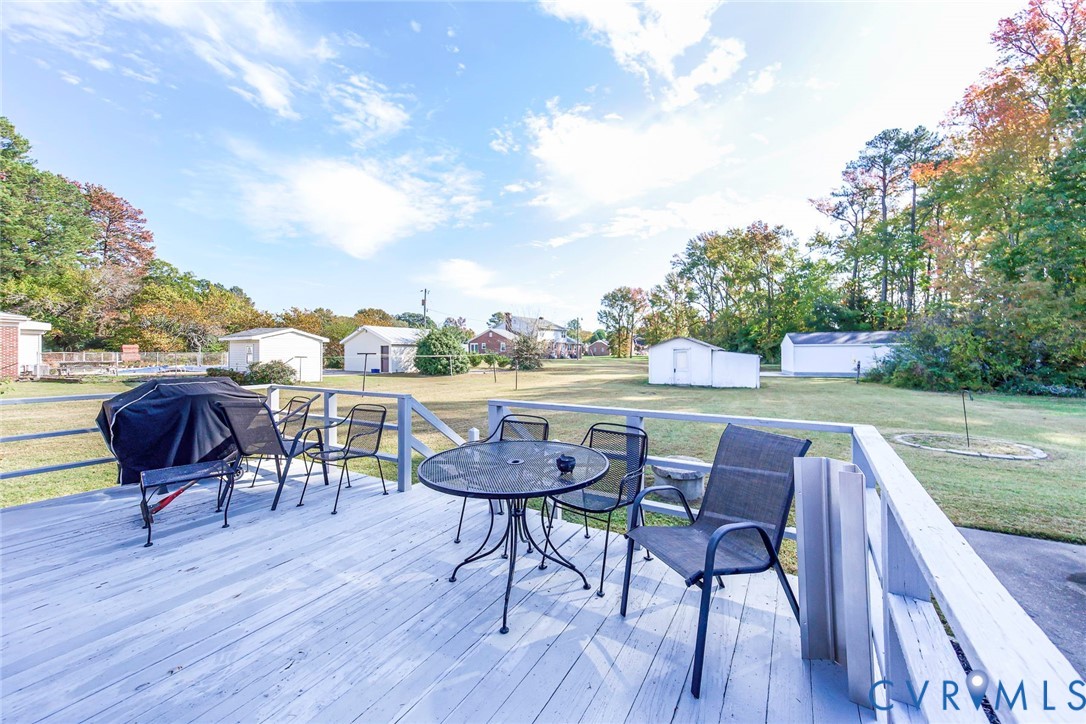 Elevated wooden deck featuring a railed perimeter, opening to an expansive backyard with mature trees and multiple detached utility structures