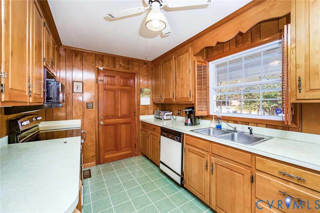 Kitchen featuring wood cabinetry, natural wood-paneled walls, solid-surface countertops, dual-basin stainless steel sink, and ceramic tile flooring