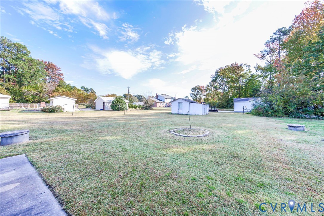 Expansive lot featuring a wide grassy expanse, mature trees, concrete perimeter structures, and multiple detached outbuildings