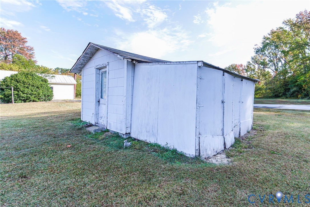 Detached outbuilding featuring white exterior siding, a gable roofline, and multiple access doors, situated on an expansive grass lot