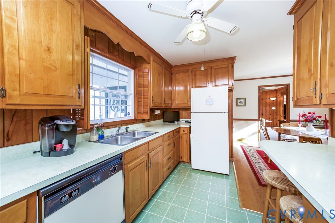 Kitchen featuring natural wood cabinetry, solid surface countertops, dual-basin stainless steel sink, tiled flooring, and a ceiling-mounted light fixture