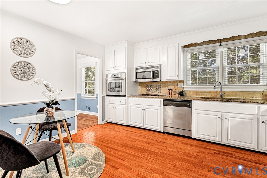Kitchen featuring white cabinetry, wood-finish flooring, stainless steel appliances including a built-in wall oven and microwave, stone-surface countertops, and multi-pane windows