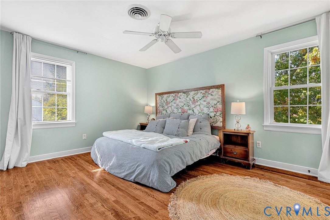 Room featuring wood-finish flooring, dual windows with muntin detailing, and a ceiling fan