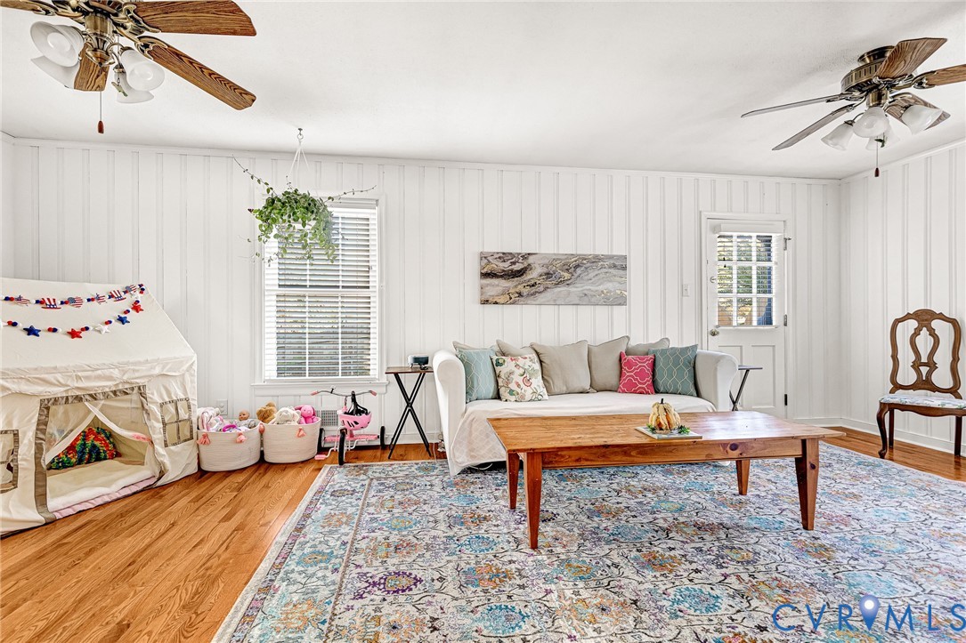 Living area featuring wood-finish flooring, vertical panel wall detailing, dual ceiling fans, and a multi-pane glass entry door
