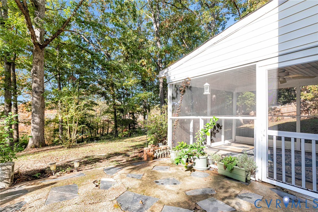 Flagstone patio featuring an integrated screen porch with white railing, ceiling fan, and surrounding mature wooded backdrop