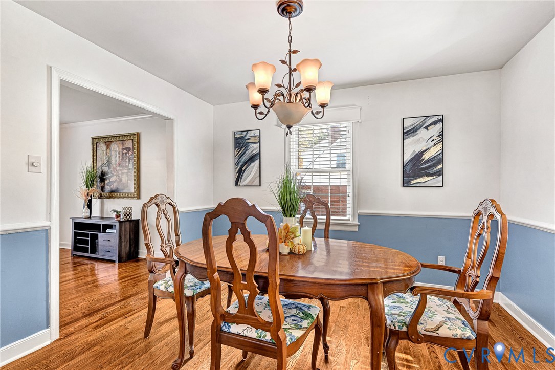 Dining area featuring wood-finish flooring, two-toned wall paint with chair rail molding, and a traditional five-light chandelier