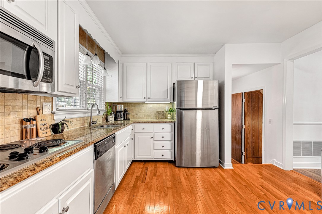 Kitchen featuring white cabinetry, stone countertops, stainless steel appliances, tiled backsplash, and wood-finish flooring