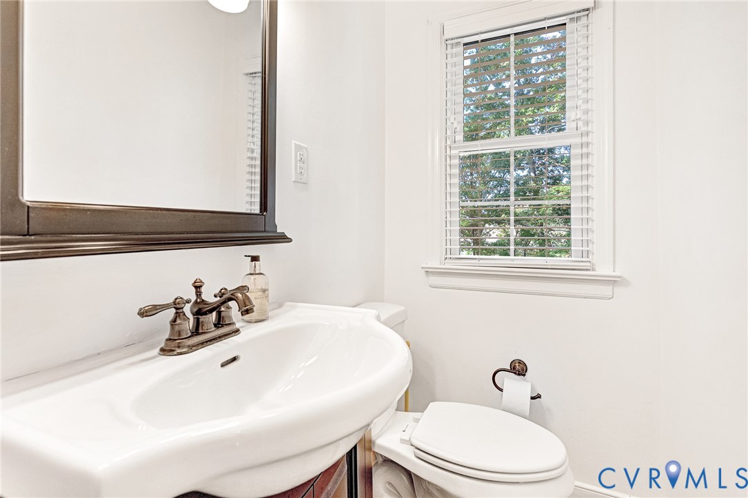 Wall-mounted mirror with a dark wood-finish frame, pedestal sink with a bronze-toned widespread faucet, and matching bronze-toned hardware