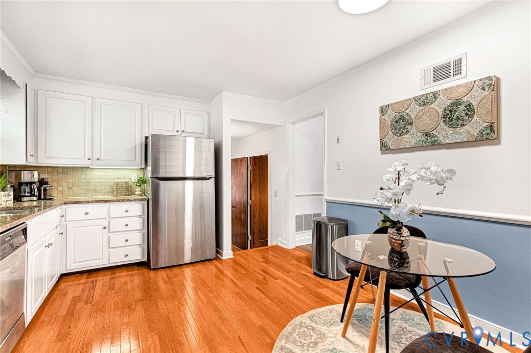 Kitchen featuring white cabinetry, stone-finish countertops, tile backsplash, stainless steel refrigerator, and wood-finish flooring