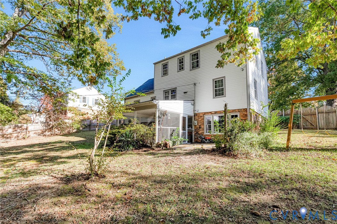 Multi-story residence featuring vinyl siding, brick foundation masonry, and a rear screened-in porch with wood framing, set upon a private lot with mature trees and perimeter wood fencing