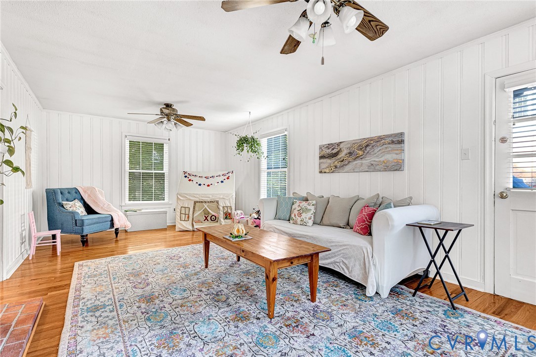 Vertical paneling, wood-finish flooring, two ceiling fans, and natural light from multi-pane windows
