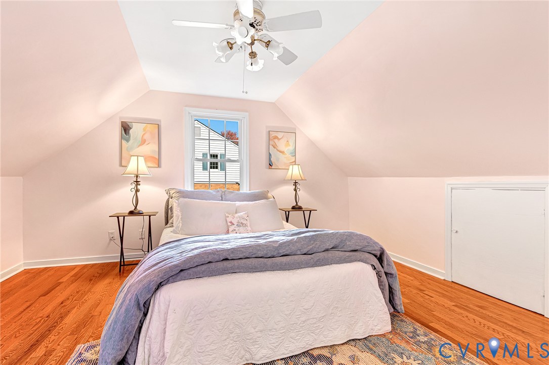Sloped ceilings featuring a central multi-light ceiling fan, polished wood-finish flooring, a multi-pane window, and built-in knee wall storage